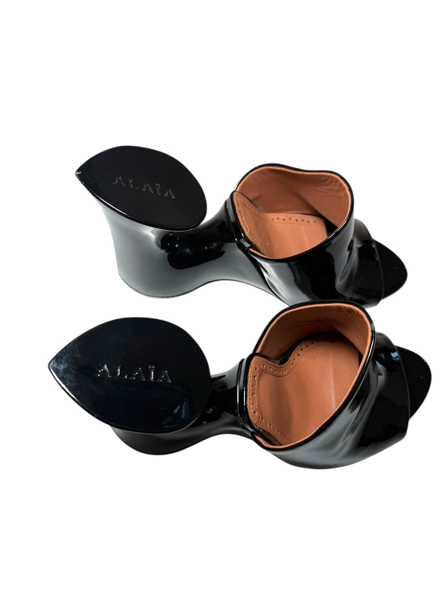 Black patent leather Alaia high-heeled mule shoes with brown insoles on a white background, featuring the brand 'Alaia' top view.