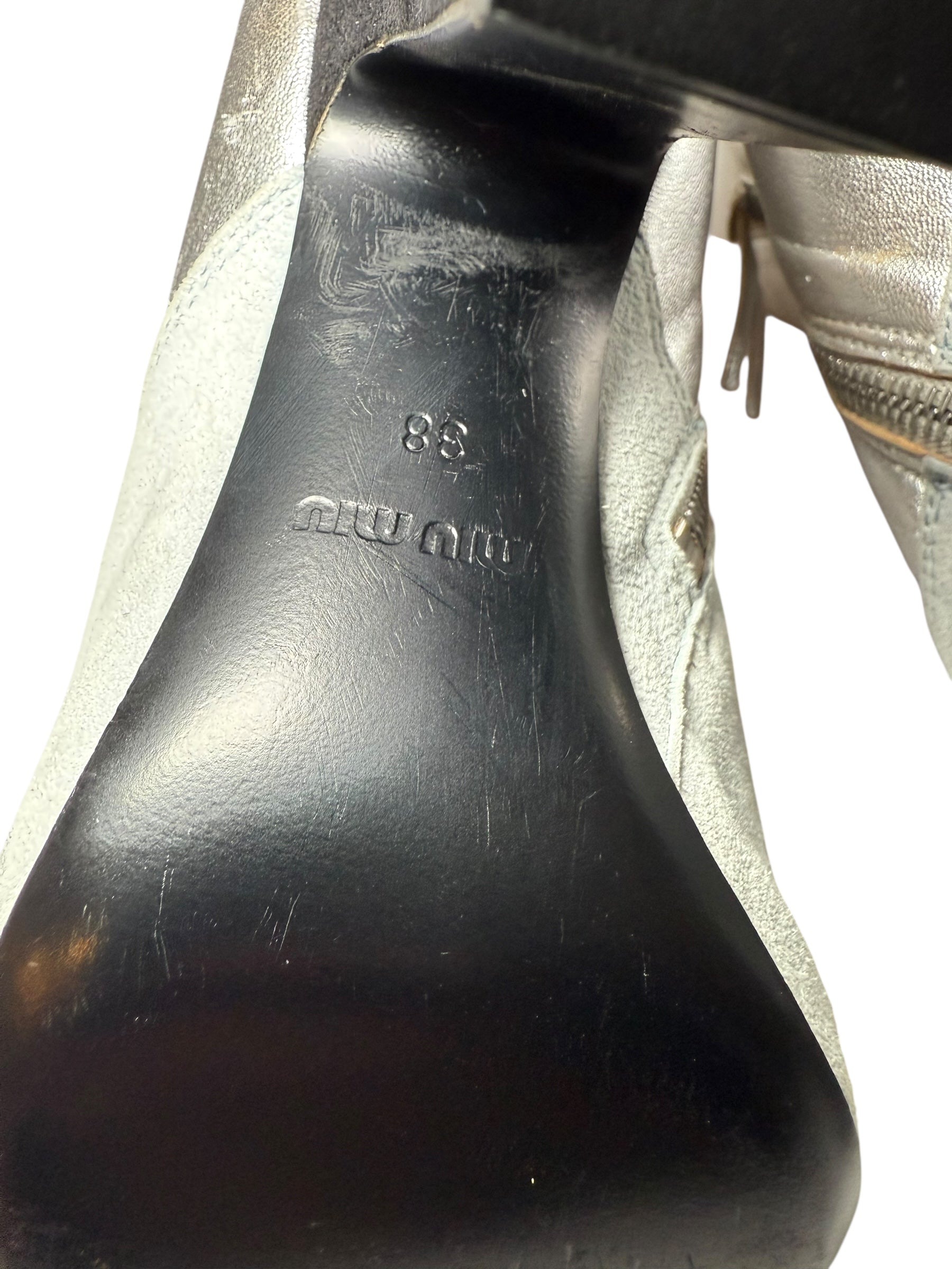 Close-up of the Miu Miu Silver Ankle Booties black shoe sole with visible wear and a Miu Miu brand logo as well sa 38 to indicate shoe size on a white background