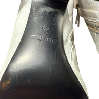 Close-up of the Miu Miu Silver Ankle Booties black shoe sole with visible wear and a Miu Miu brand logo as well sa 38 to indicate shoe size on a white background