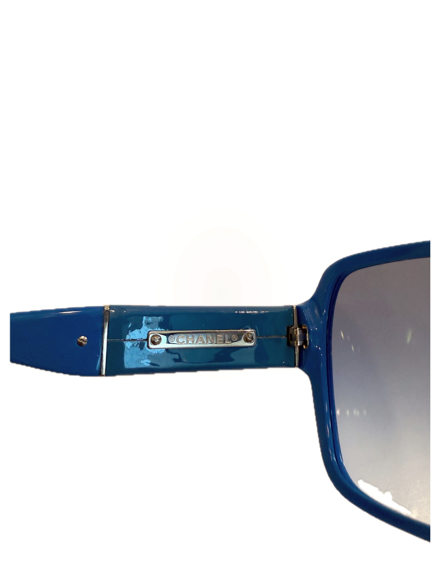 Close-up of Chanel metal logo plate on blue sunglasses temple.