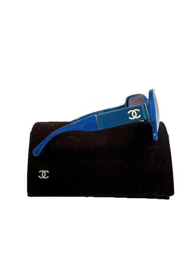 Side view of Chanel blue sunglasses showing white CC logo and wide temple on black case.