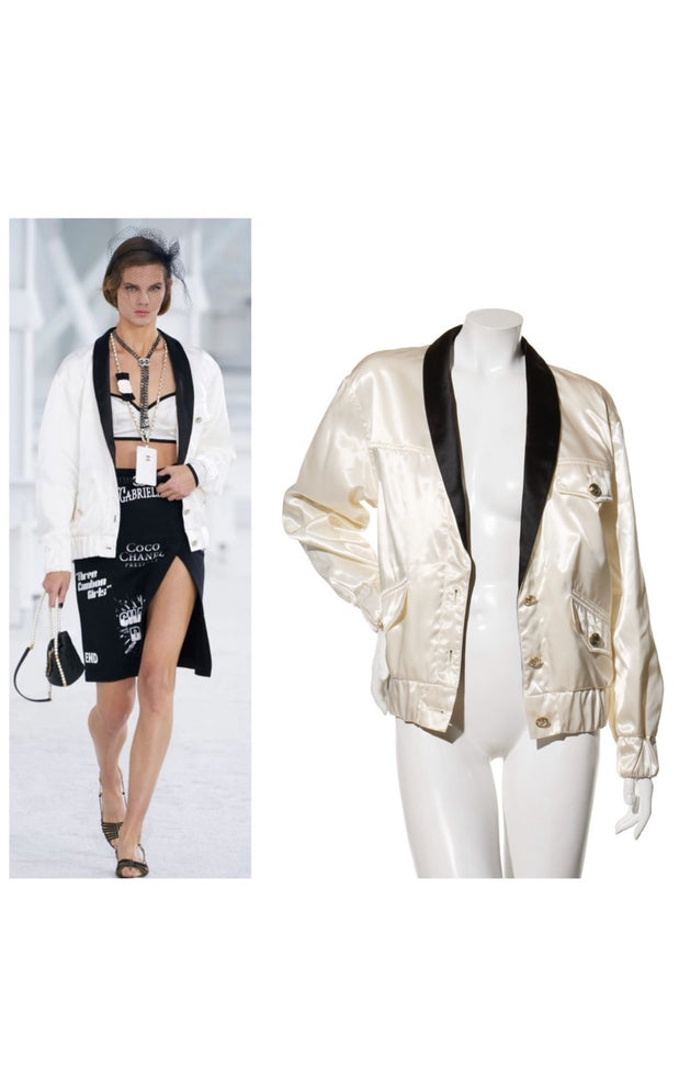 Chanel cream satin jacket on a mannequin with a model on the Chanel Cruise 2021 Collection runway show modeling the jacket in the background.