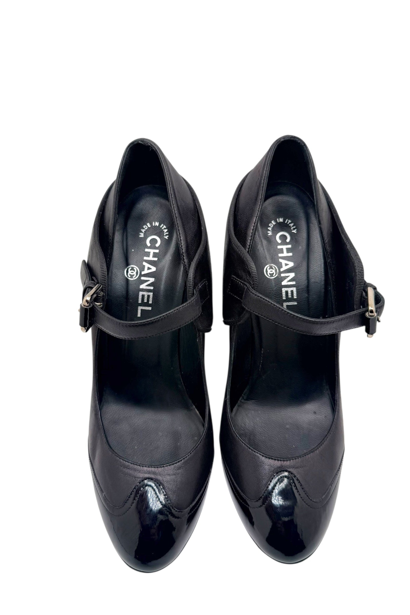 Top view close-up of Chanel black leather Mary Jane pumps with patent toe caps and strap closure.