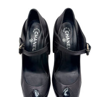 Top view close-up of Chanel black leather Mary Jane pumps with patent toe caps and strap closure.