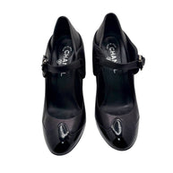Top view of Chanel black leather Mary Jane pumps with patent toe caps and strap closure.