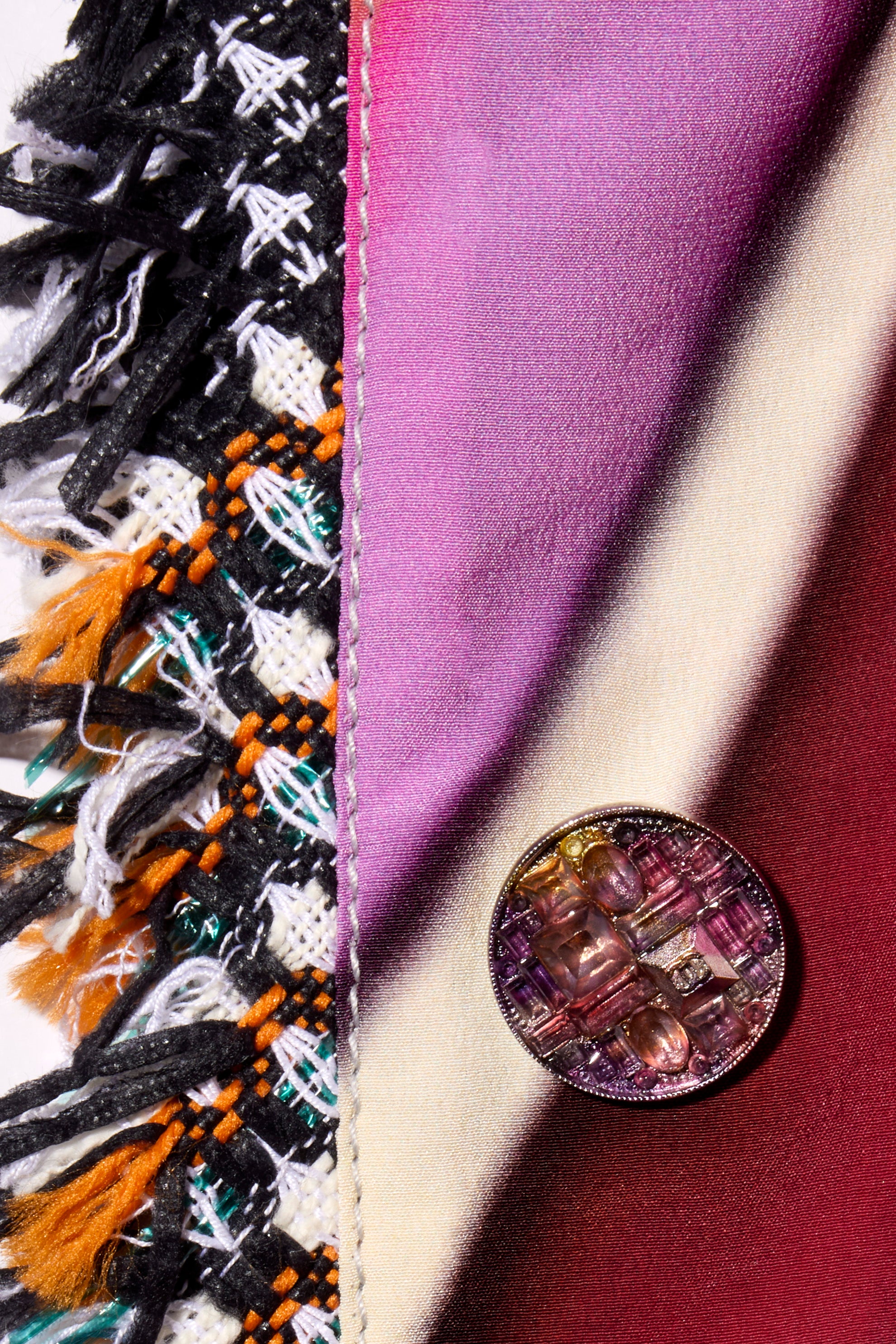 Close-up of Chanel reversible coat decorative button on fabric with fringe and floral print detail.
