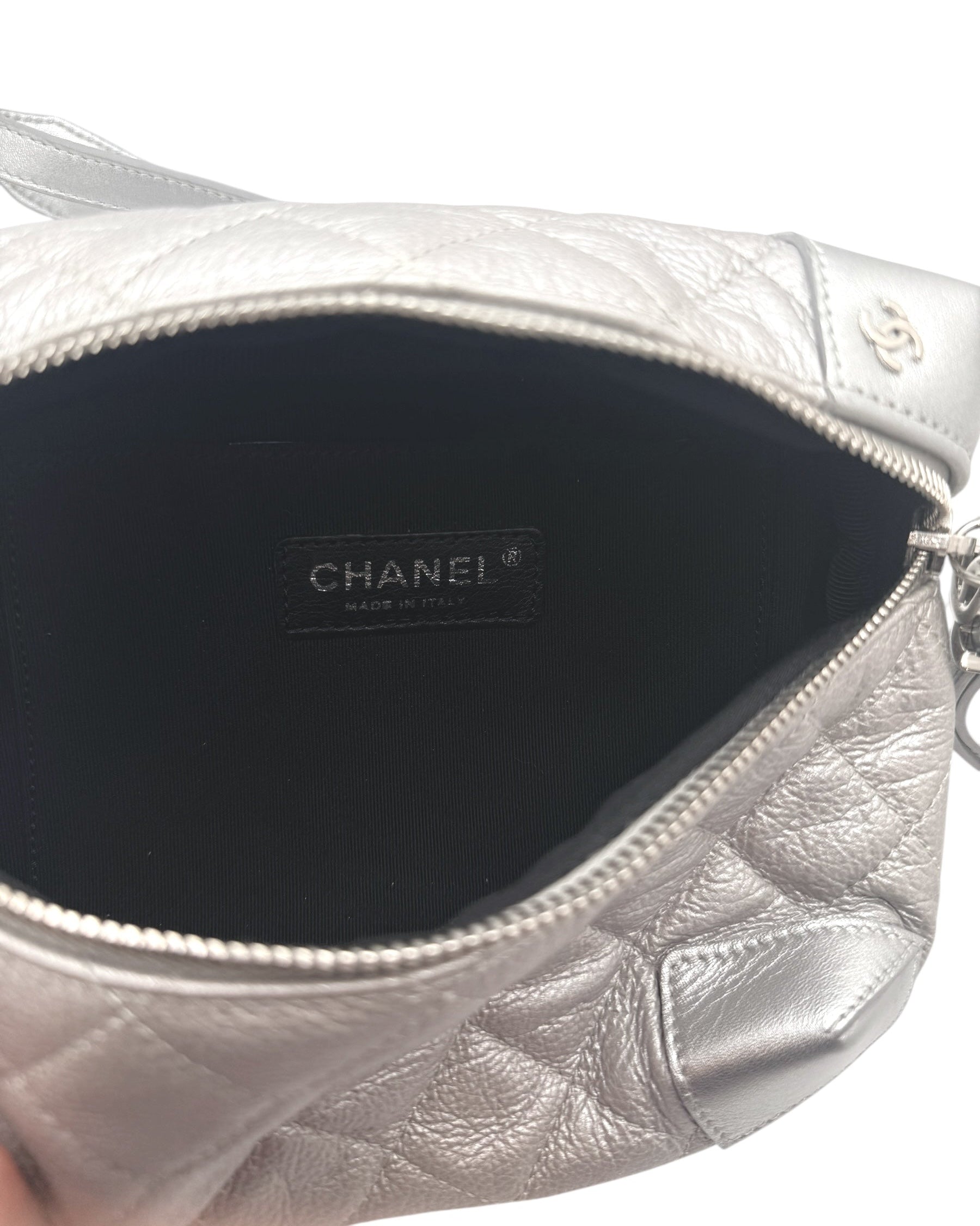Interior view of Chanel metallic silver quilted bum bag showing Chanel Made in Italy leather label and black fabric lining.
