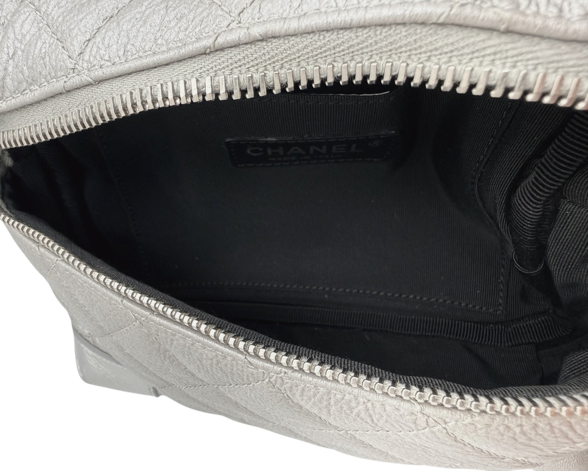 Wide interior view of Chanel metallic silver quilted bum bag showing spacious compartment, zip opening, and black fabric lining.