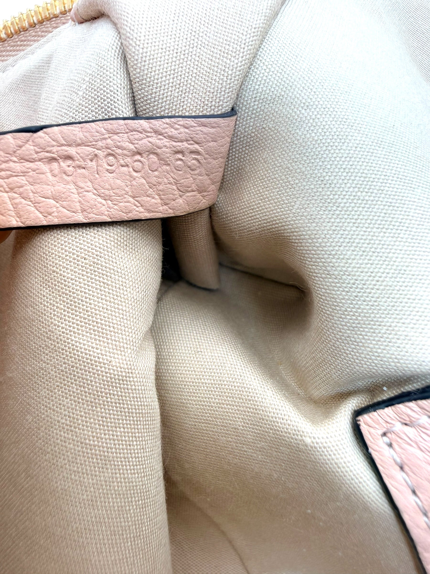 Close-up of interior authenticity date code stamp on leather tag inside Chloé Alphabet blush leather pouch.