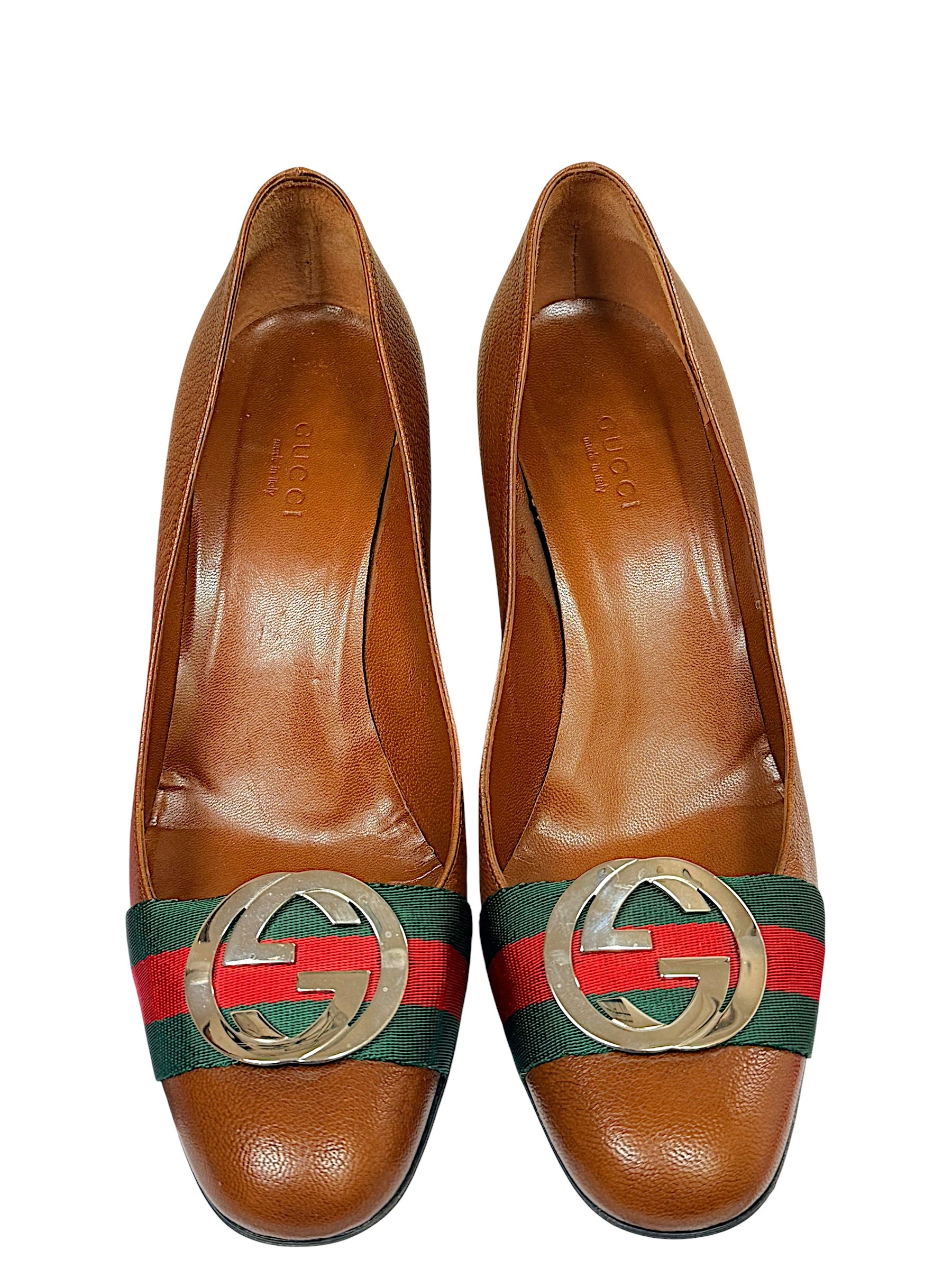 Close-up front view of Gucci brown pebbled leather pumps with signature Web stripe and oversized GG logo hardware.