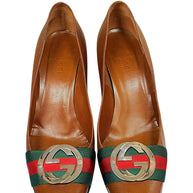 Close-up front view of Gucci brown pebbled leather pumps with signature Web stripe and oversized GG logo hardware.