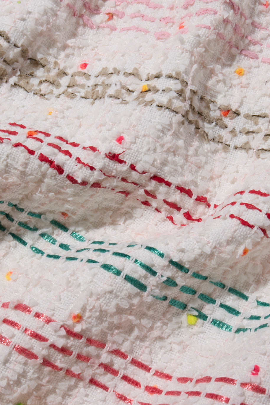 Close-up of multi color tweed fabric with red and green interwoven stitching on a white background of Chanel 2019 Tweed Coat