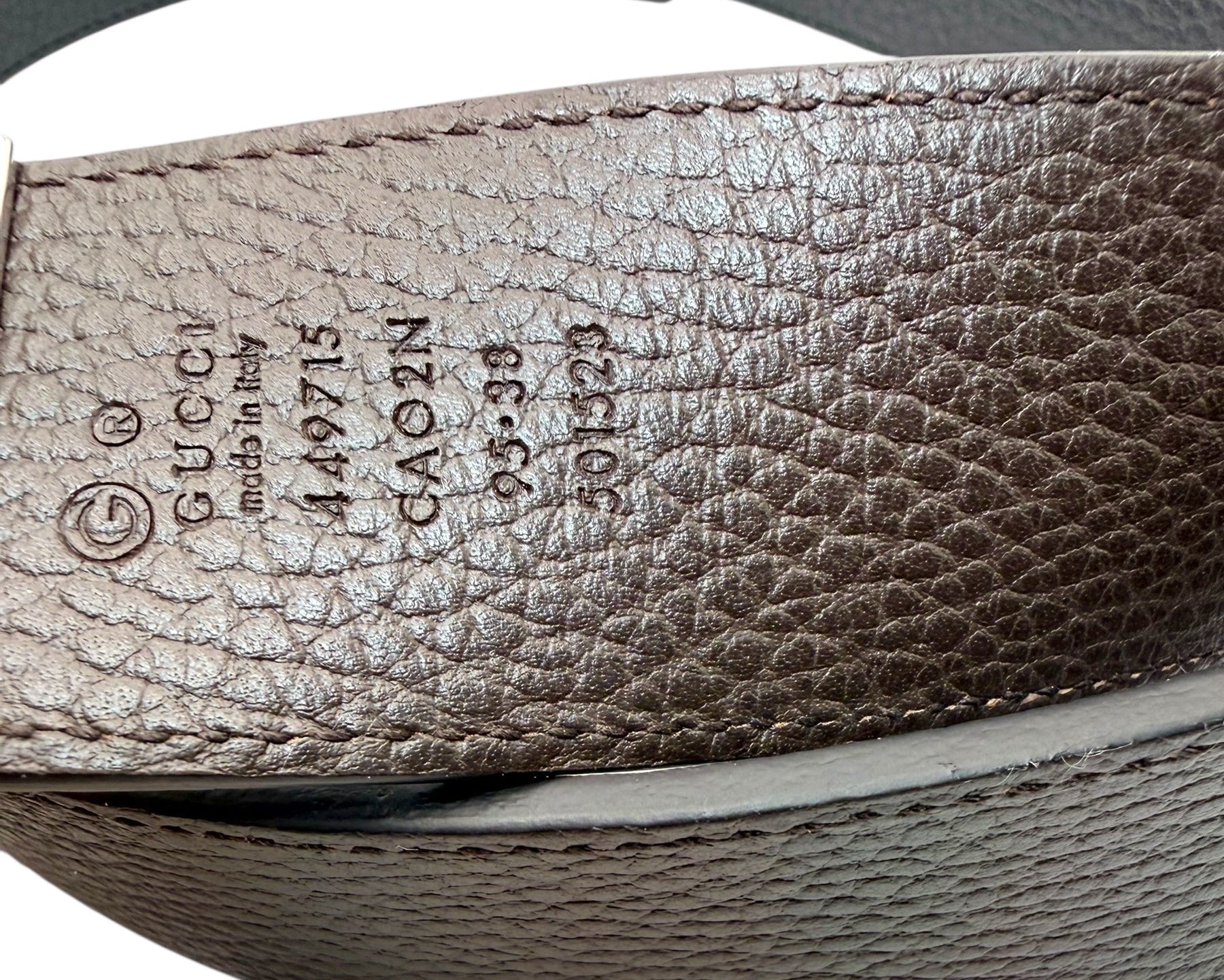 Close-up of reversible brown leather Gucci belt with visible branding and numbers.
