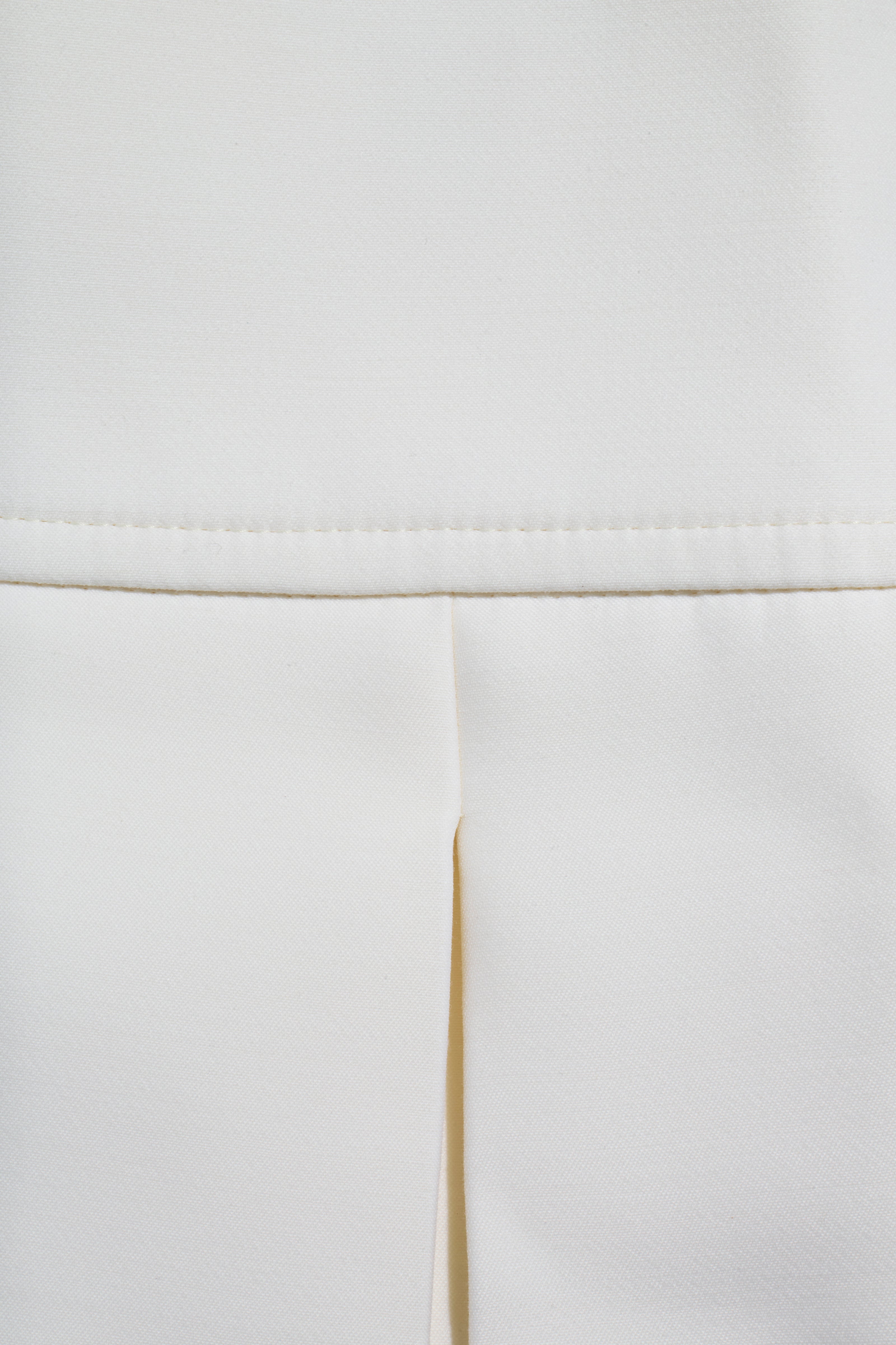 Detailed close-up of the Louis Vuitton white mini skirt showing the structured pleat and midweight fabric texture.