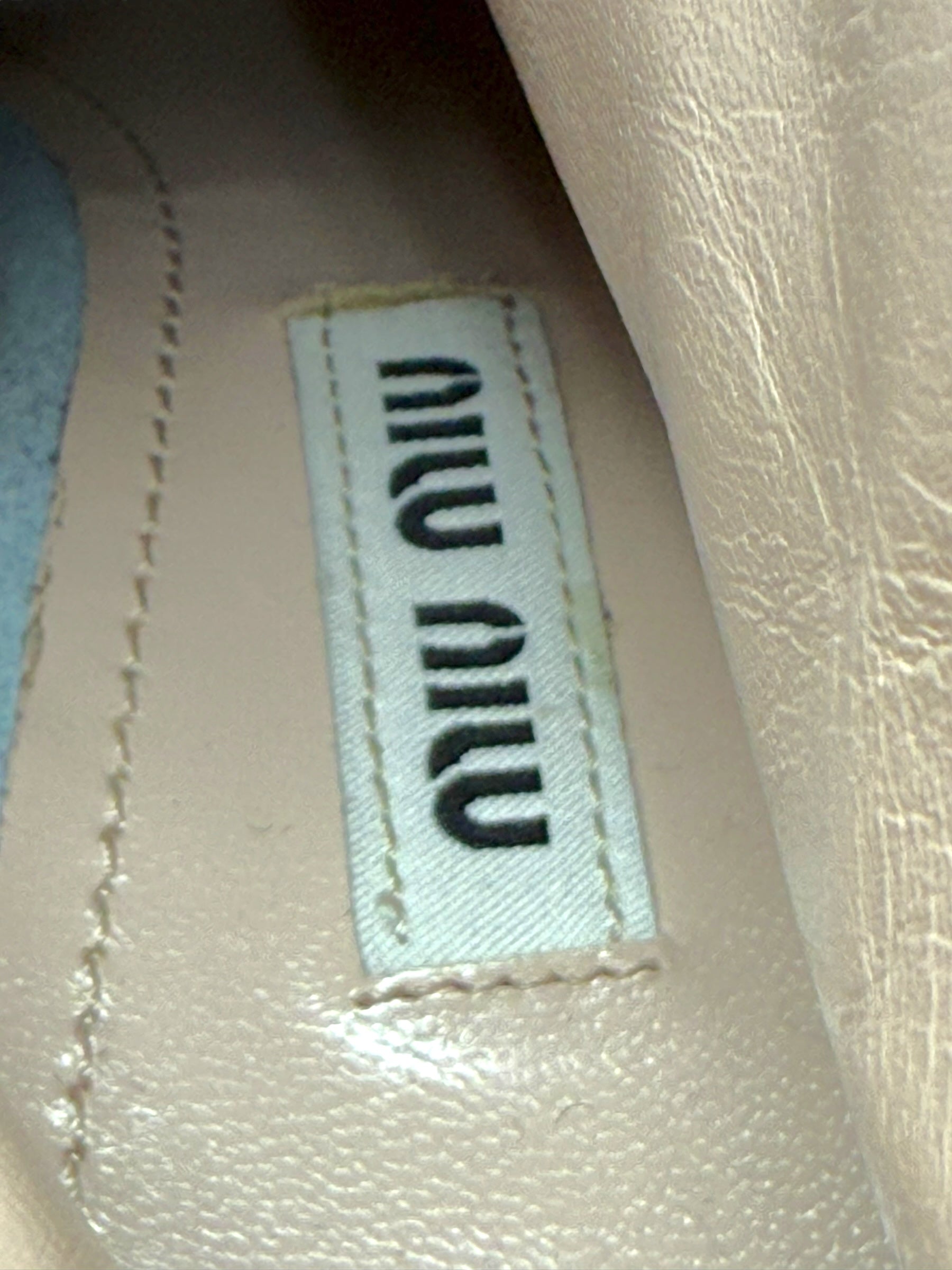 Close-up of Designer label with 'MIU MIU' branding on a textured surface on the inside sole of the silver metallic ankle booties..