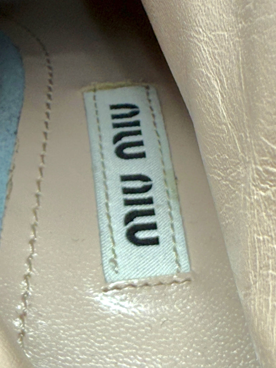 Close-up of Designer label with 'MIU MIU' branding on a textured surface on the inside sole of the silver metallic ankle booties..