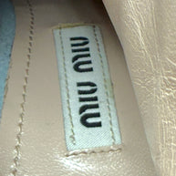 Close-up of Designer label with 'MIU MIU' branding on a textured surface on the inside sole of the silver metallic ankle booties..