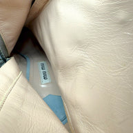 Close-up of a beige leather interior of the silver Miu Miu booties with the visible Miu Miu brand label.