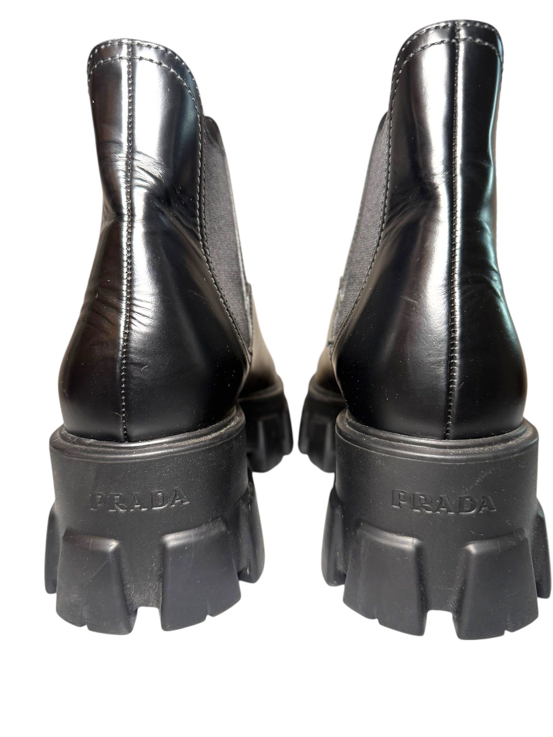 Black Prada boots with close up of Prada label stamped into back heels of the thick soles on a white background