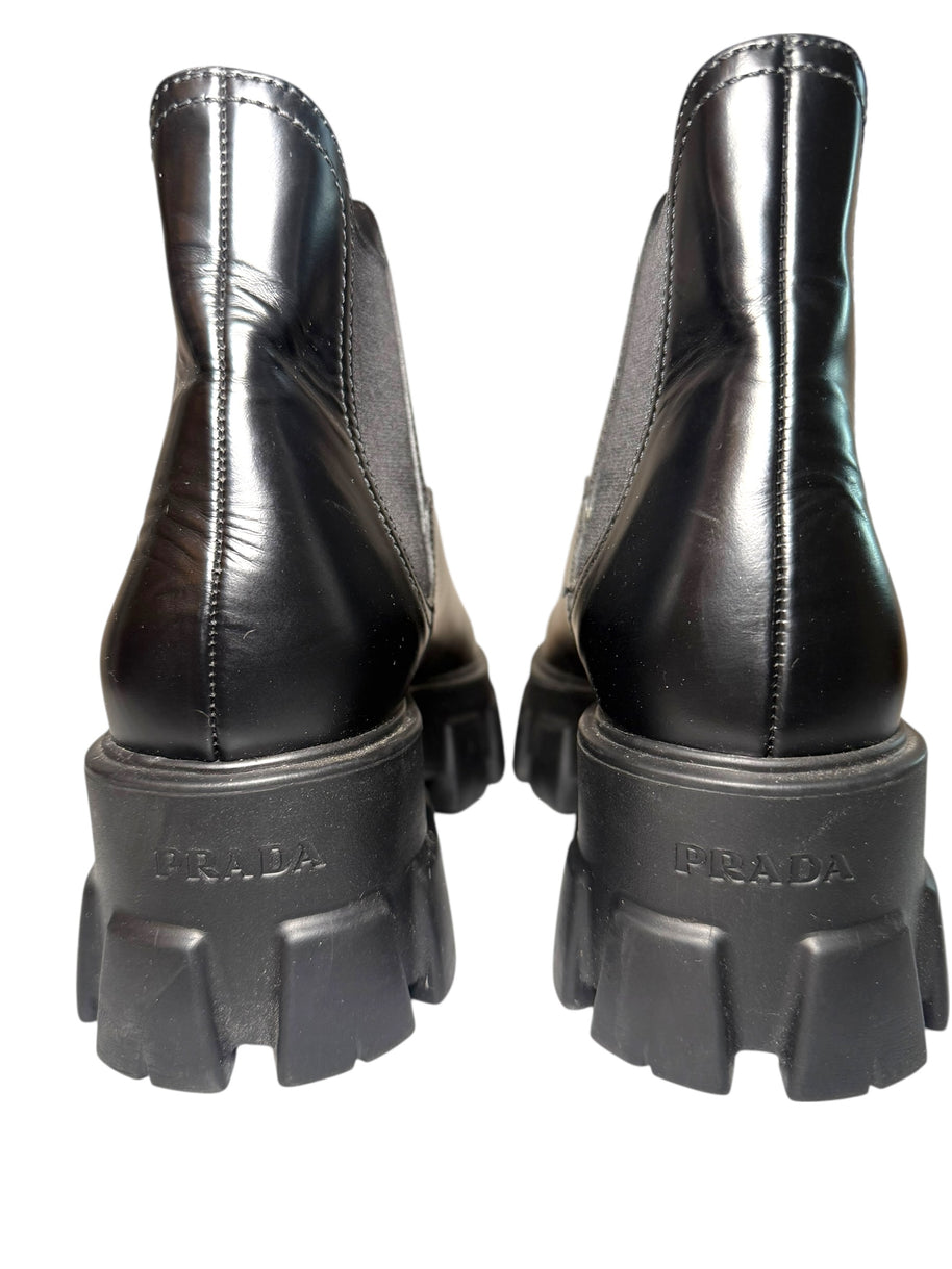 Black Prada boots with close up of Prada label stamped into back heels of the thick soles on a white background