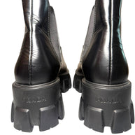 Black Prada boots with close up of Prada label stamped into back heels of the thick soles on a white background