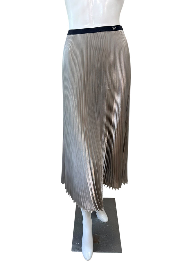 Front view of Prada metallic pleated midi skirt in champagne silver with fluid plissé fabric and black elastic Prada Milano logo waistband.