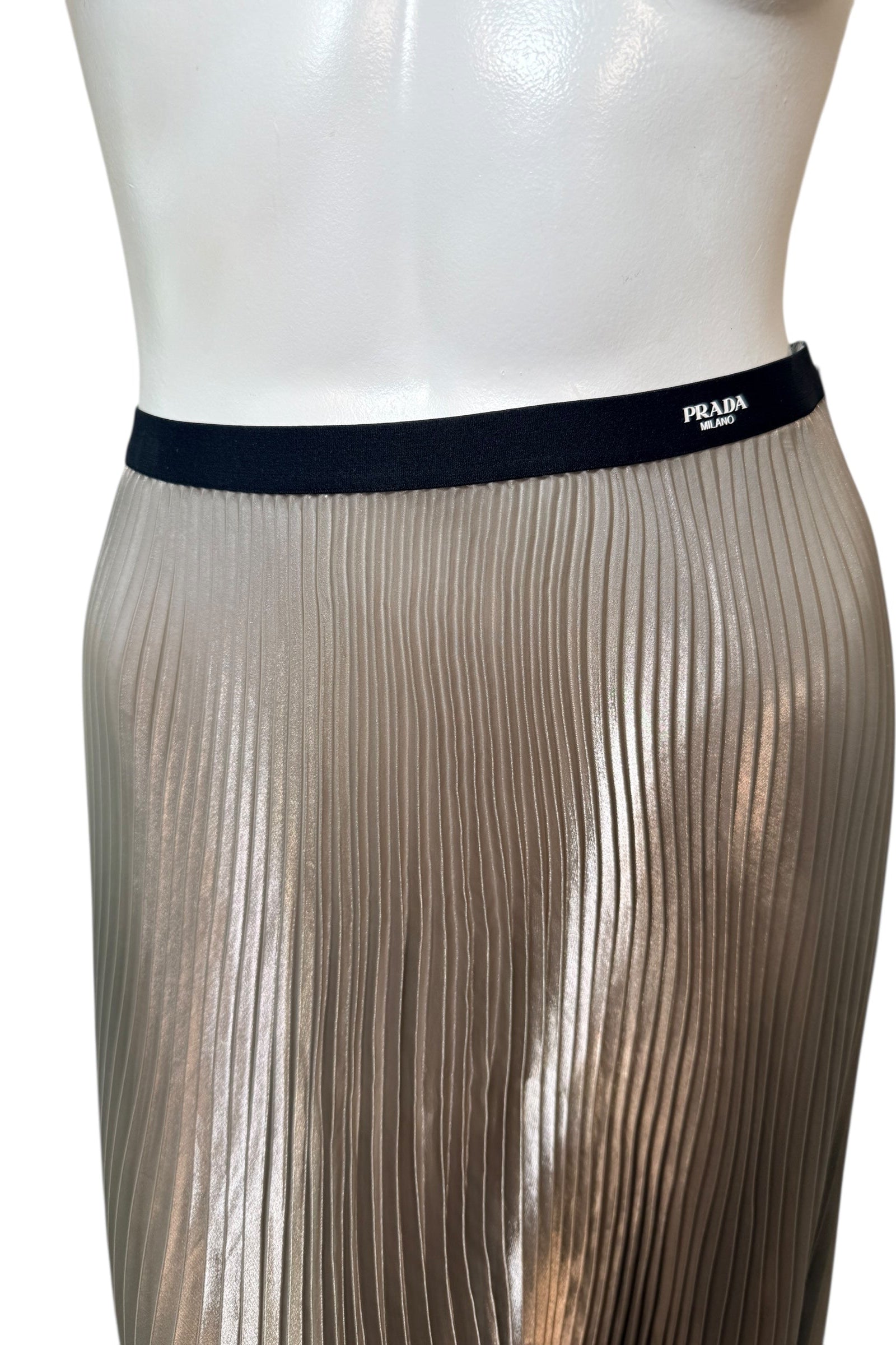 Detailed view of Prada Milano logo woven into black elastic waistband on metallic pleated skirt.