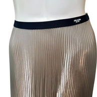 Detailed view of Prada Milano logo woven into black elastic waistband on metallic pleated skirt.