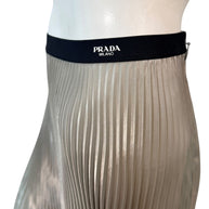 Detailed close-up side view of Prada Milano logo woven into black elastic waistband on metallic pleated skirt.