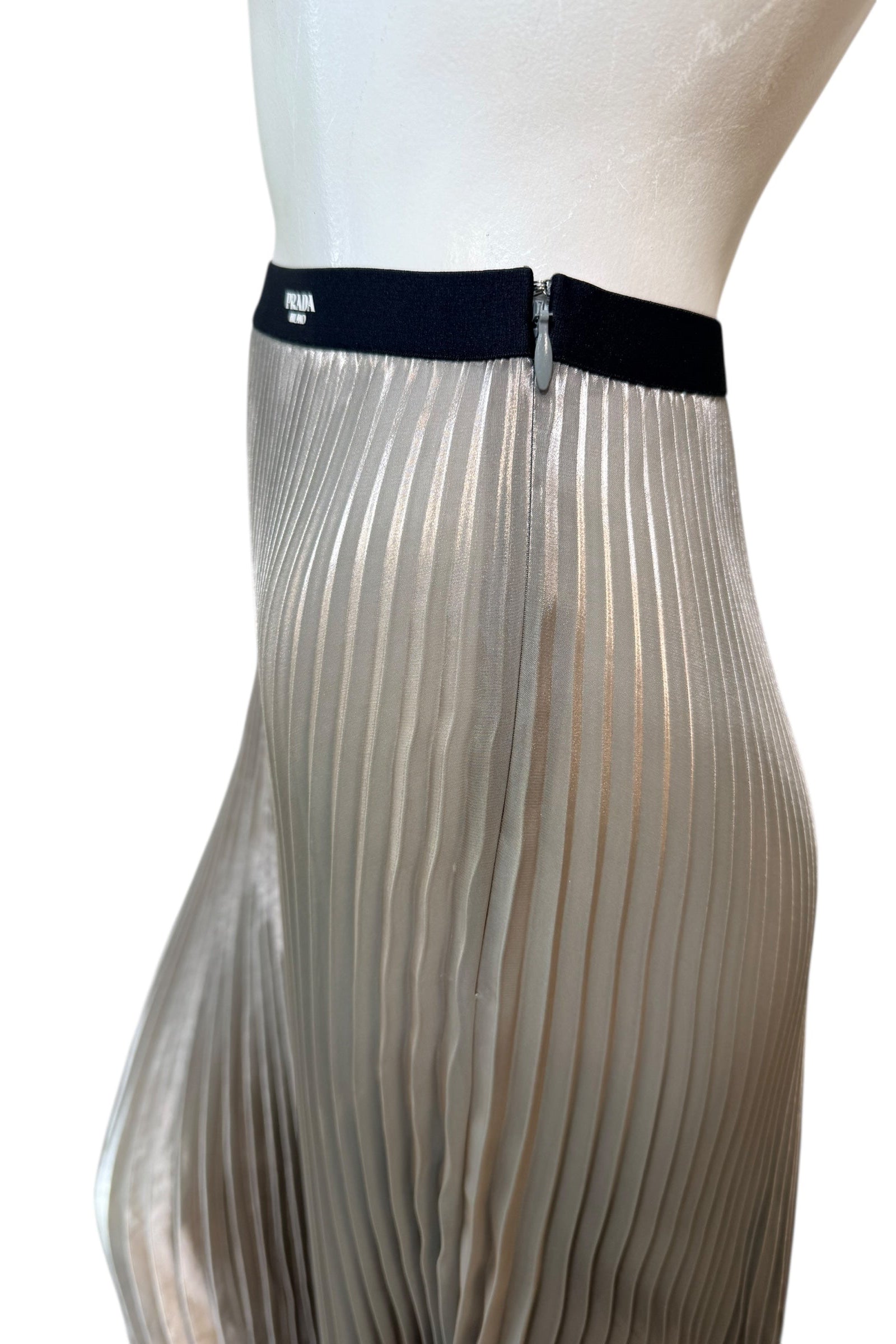 Close-up of Prada metallic pleated skirt showing elastic Prada Milano logo waistband and concealed zipper detail.