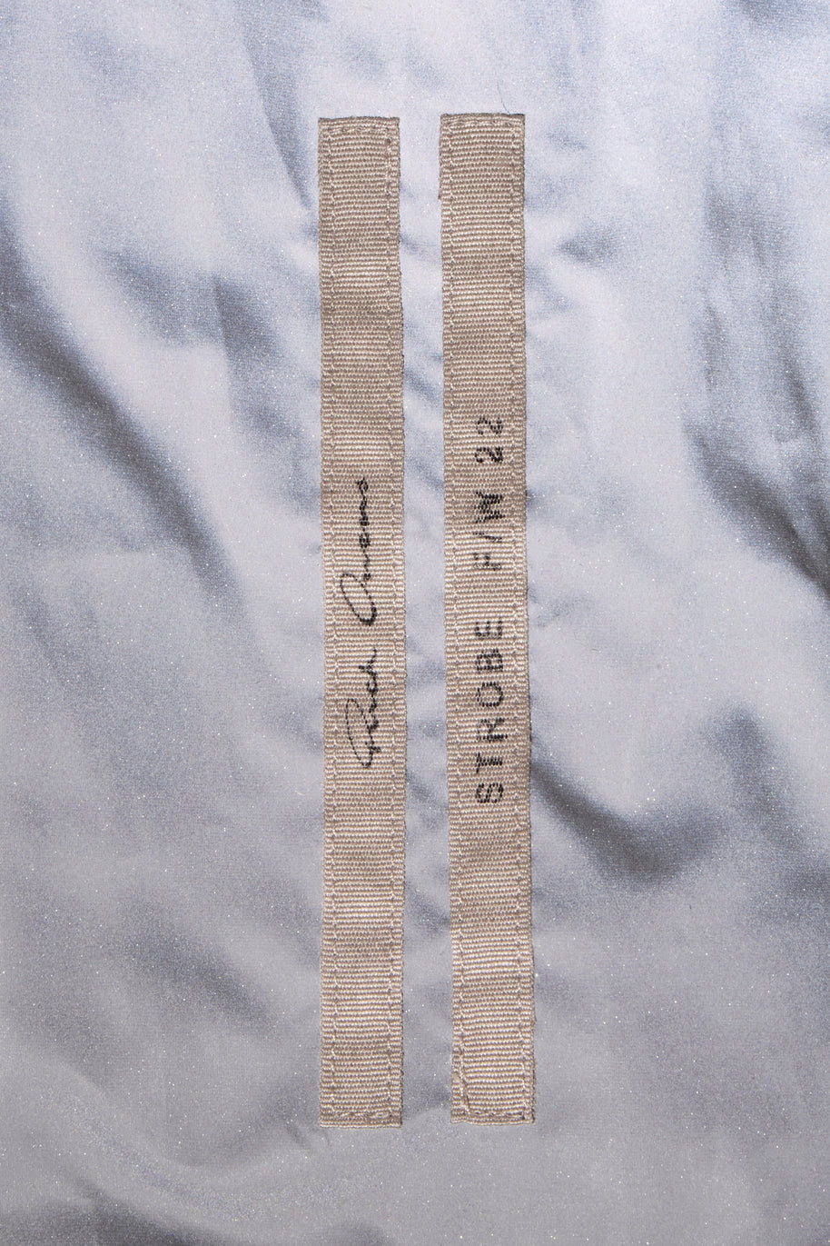 Rick Owens brand label of two strips with brand logo on one strip and the collection and year on the second strip attached to the interior of the metallic gray cropped bomber jacket from the FW22 Strobe collection.