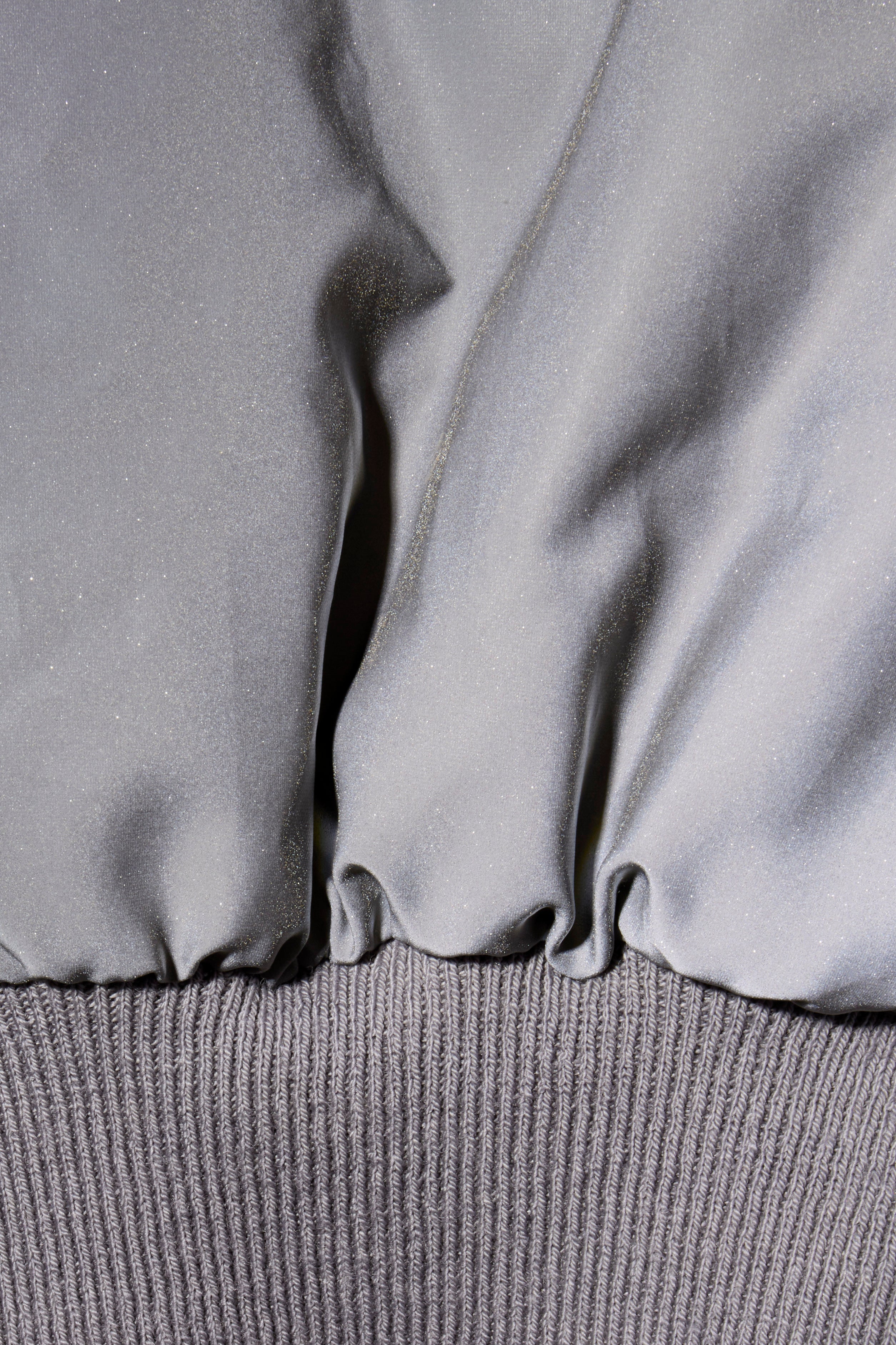 Rick Owens Bomber Jacket Close-up of a metallic gray fabric texture with ribbed waist band on FW22 Strobe jacket.