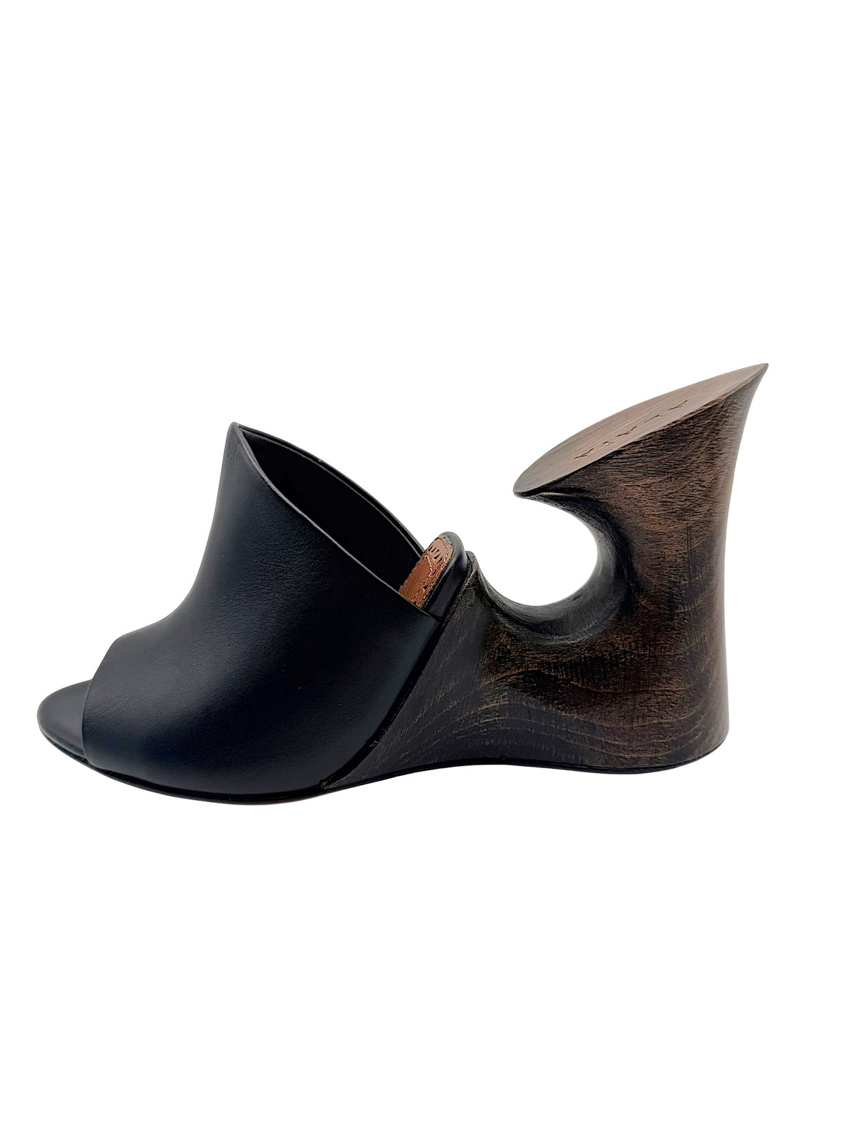 Side view of Alaïa La Sculpture black leather mule highlighting the curved wooden wedge construction and circular heel opening.
