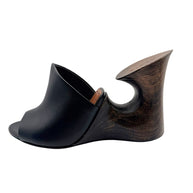 Side view of Alaïa La Sculpture black leather mule highlighting the curved wooden wedge construction and circular heel opening.