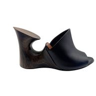 Side profile of an Alaïa La Sculpture black leather mule showing its architectural wooden wedge heel with circular cutout.