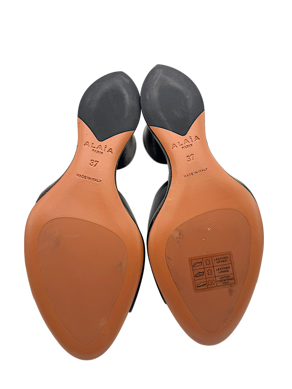 Bottom view of Alaïa La Sculpture black leather mules showing Alaïa Paris branding, EU size 37, Made in Italy markings and leather outsoles with light surface wear.