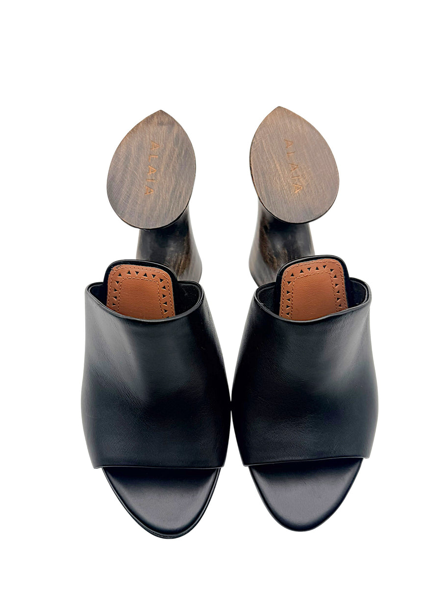 Overhead view of Alaïa La Sculpture black leather open-toe mules with cognac leather insoles and engraved Alaïa wooden heels.