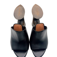 Overhead view of Alaïa La Sculpture black leather open-toe mules with cognac leather insoles and engraved Alaïa wooden heels.