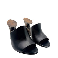 Angled front view of Alaïa La Sculpture black leather mules with wide leather uppers, open toes and sculptural wooden wedge heels.