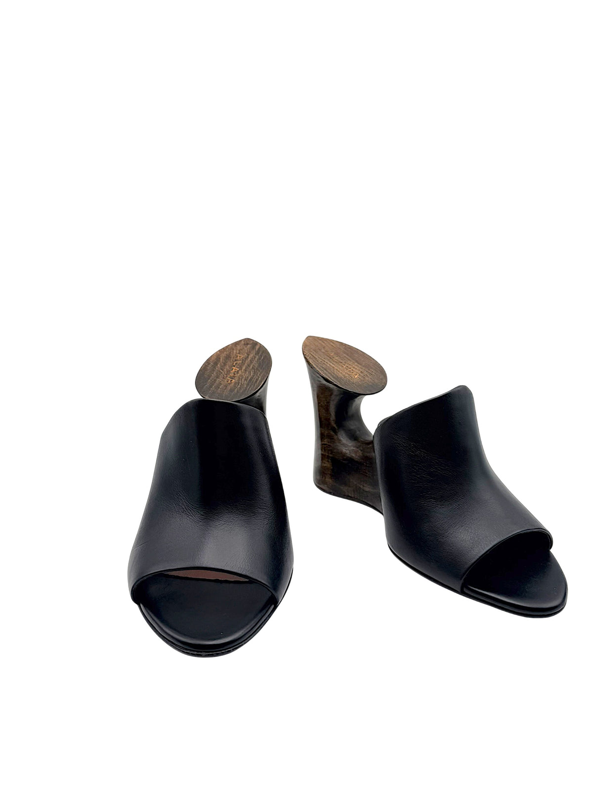 Alaïa La Sculpture black leather open-toe mules in front three-quarter view, featuring architectural dark wood cutout wedge heels.