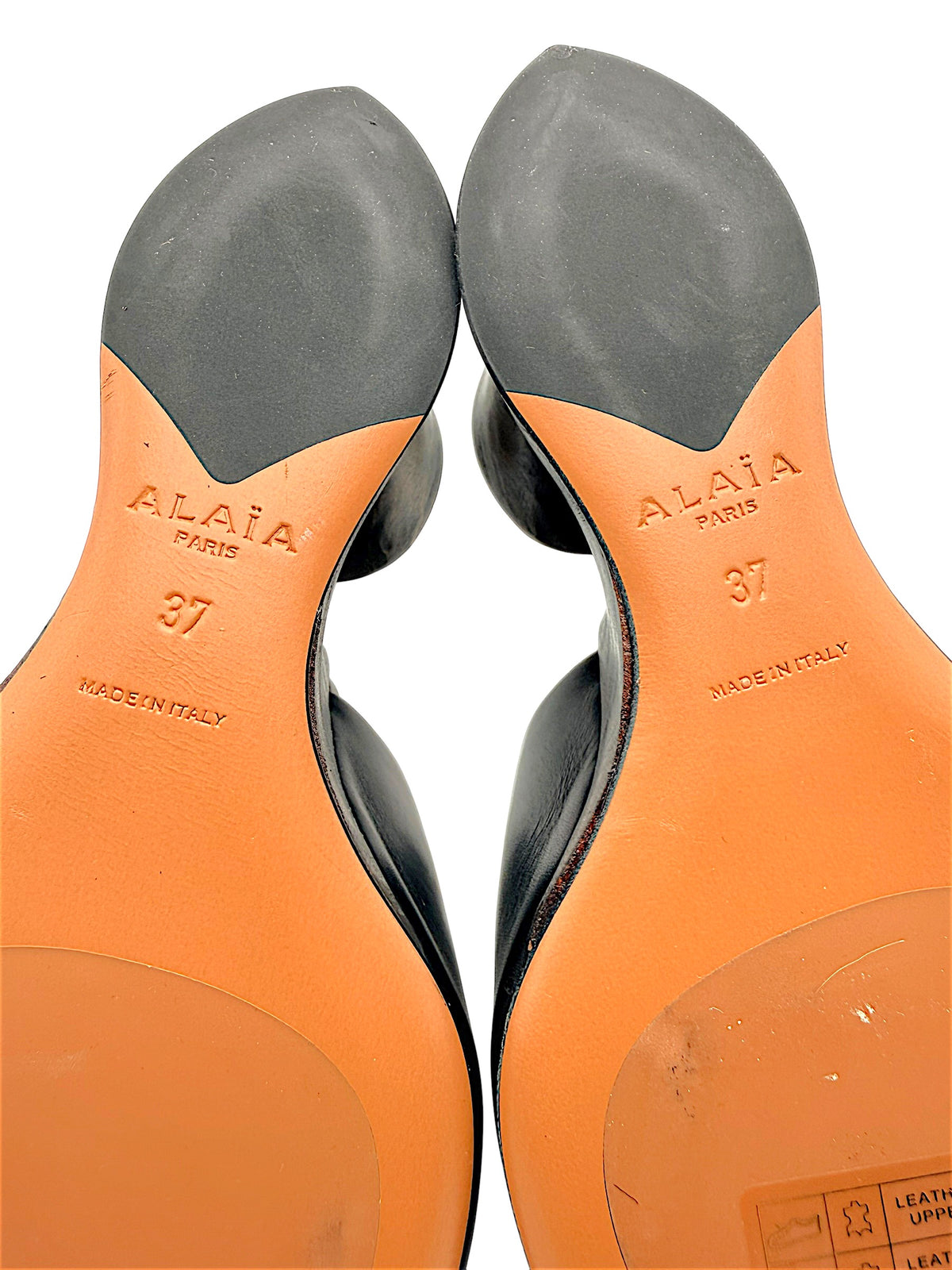 Detailed close-up of Alaïa La Sculpture mule outsoles showing embossed Alaïa Paris logos, European size 37, Made in Italy stamps and rubber traction sections.