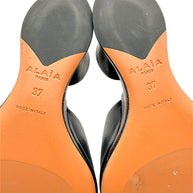 Detailed close-up of Alaïa La Sculpture mule outsoles showing embossed Alaïa Paris logos, European size 37, Made in Italy stamps and rubber traction sections.