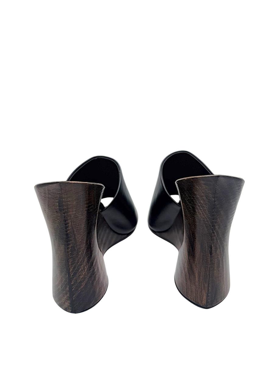 Rear view of Alaïa La Sculpture mules highlighting the curved dark-stained wooden wedge heels and natural wood grain.
