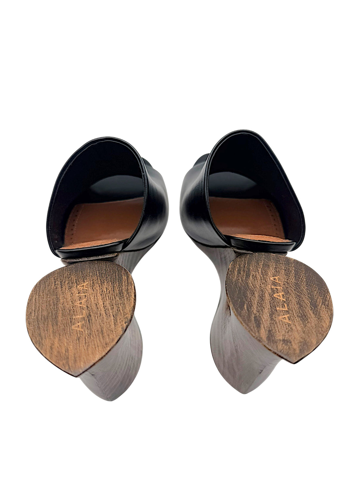 Close-up of Alaïa La Sculpture mules showing Alaïa engraved wooden heel bases, black leather uppers and cognac leather insoles.