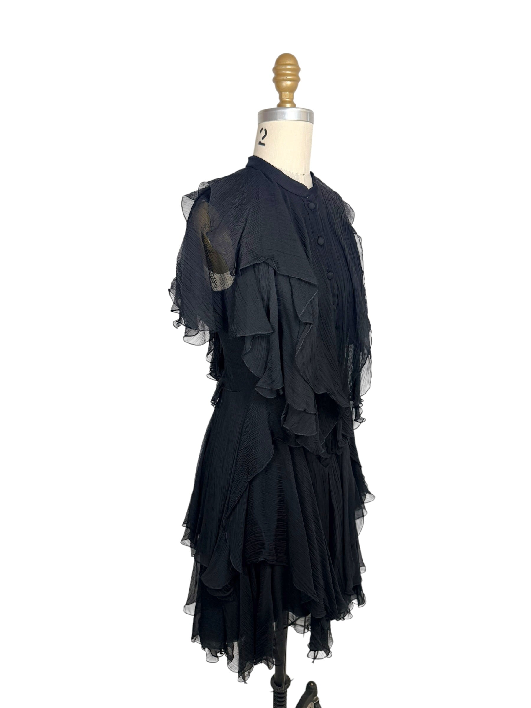 Left three-quarter view of an Alexander McQueen Pre-Fall 2016 black silk chiffon dress with layered ruffles, pleated texture, and sheer flutter sleeves.