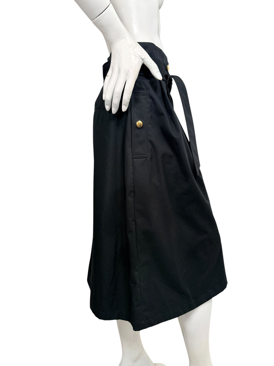 Side profile of Celine black cotton belted midi skirt showing gold-tone button pocket detail and below-the-knee silhouette.