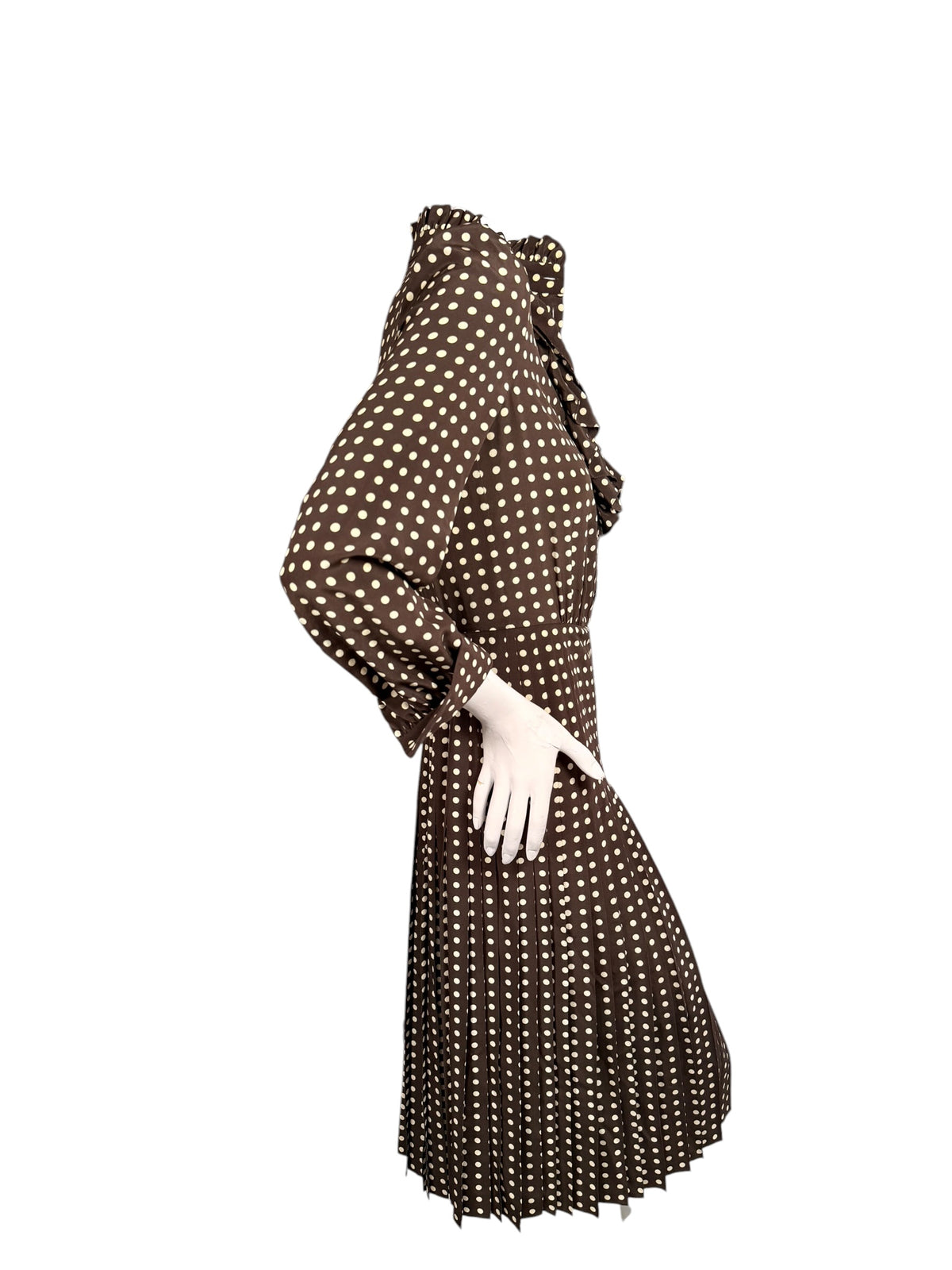 Side view of Celine FW 2020 brown polka dot silk dress highlighting its fitted waist, long sleeve, ruffled neckline and pleated skirt.