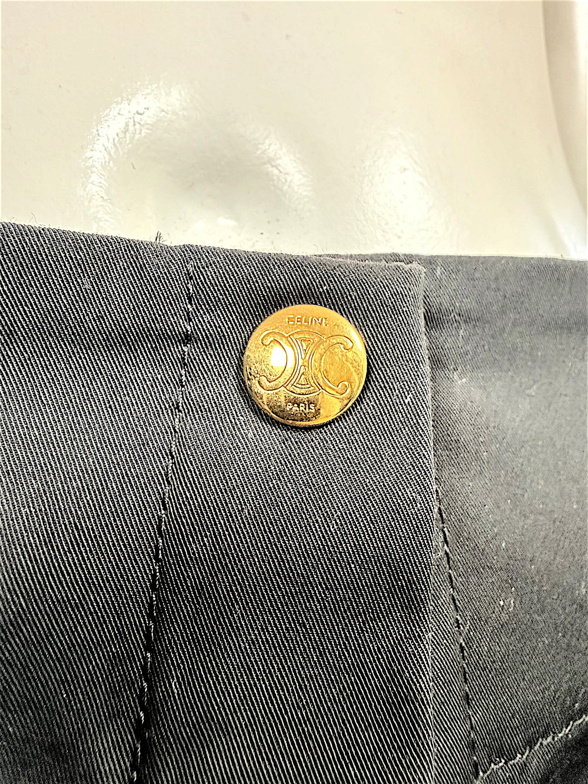 Detailed close-up of Celine Paris gold-tone Triomphe emblem button on black cotton fabric, showing engraved designer branding.
