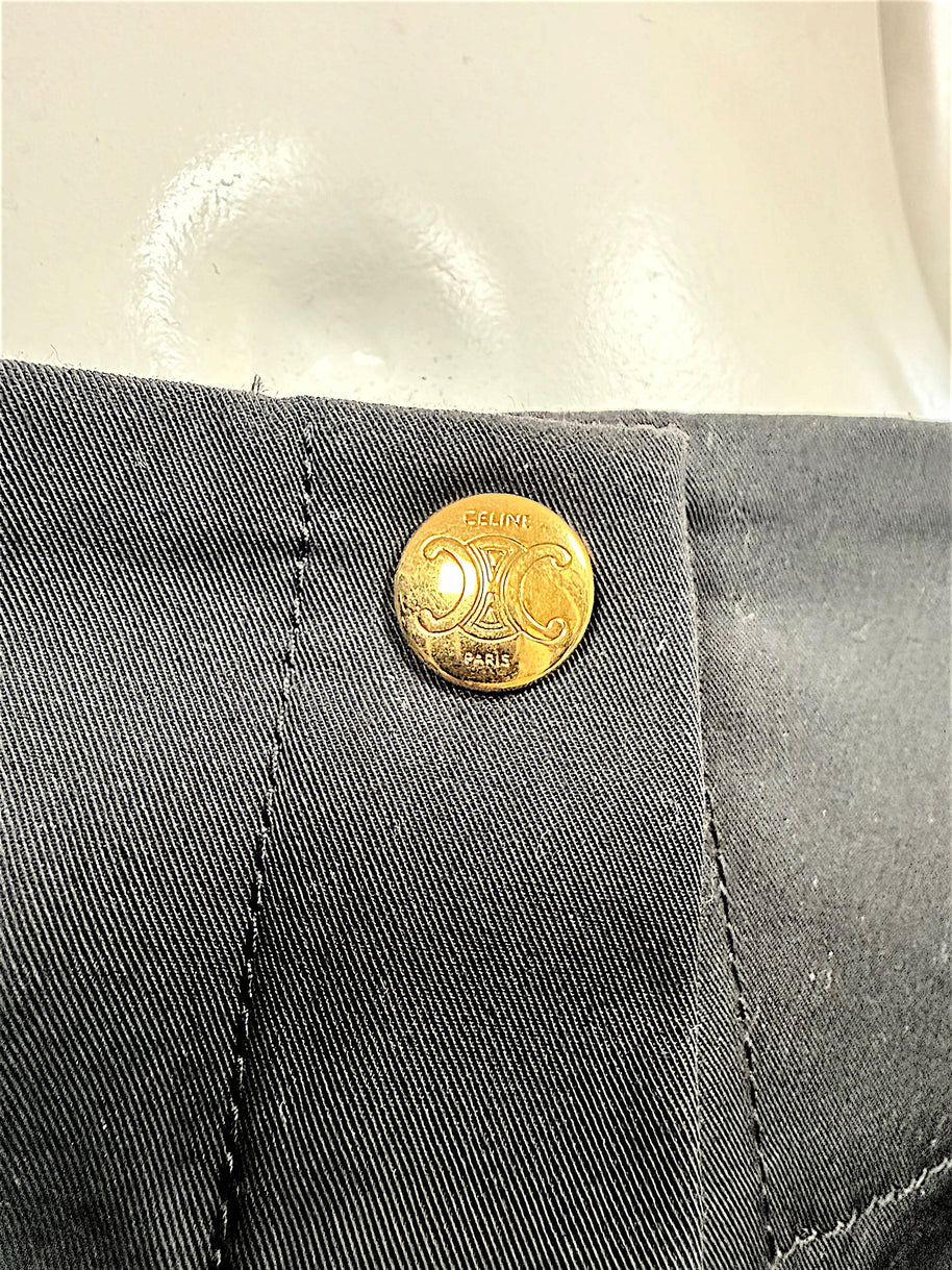 Detailed close-up of Celine Paris gold-tone Triomphe emblem button on black cotton fabric, showing engraved designer branding.