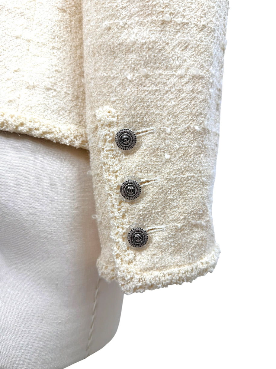 Close-up detail of engraved silver-tone Chanel CC buttons on ivory bouclé jacket cuff